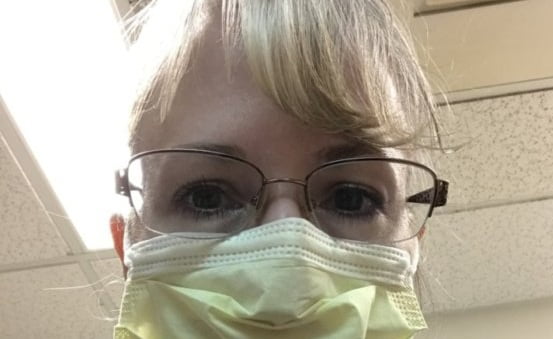 Photo of a woman wearing glasses and a yellow face mask for infection control.