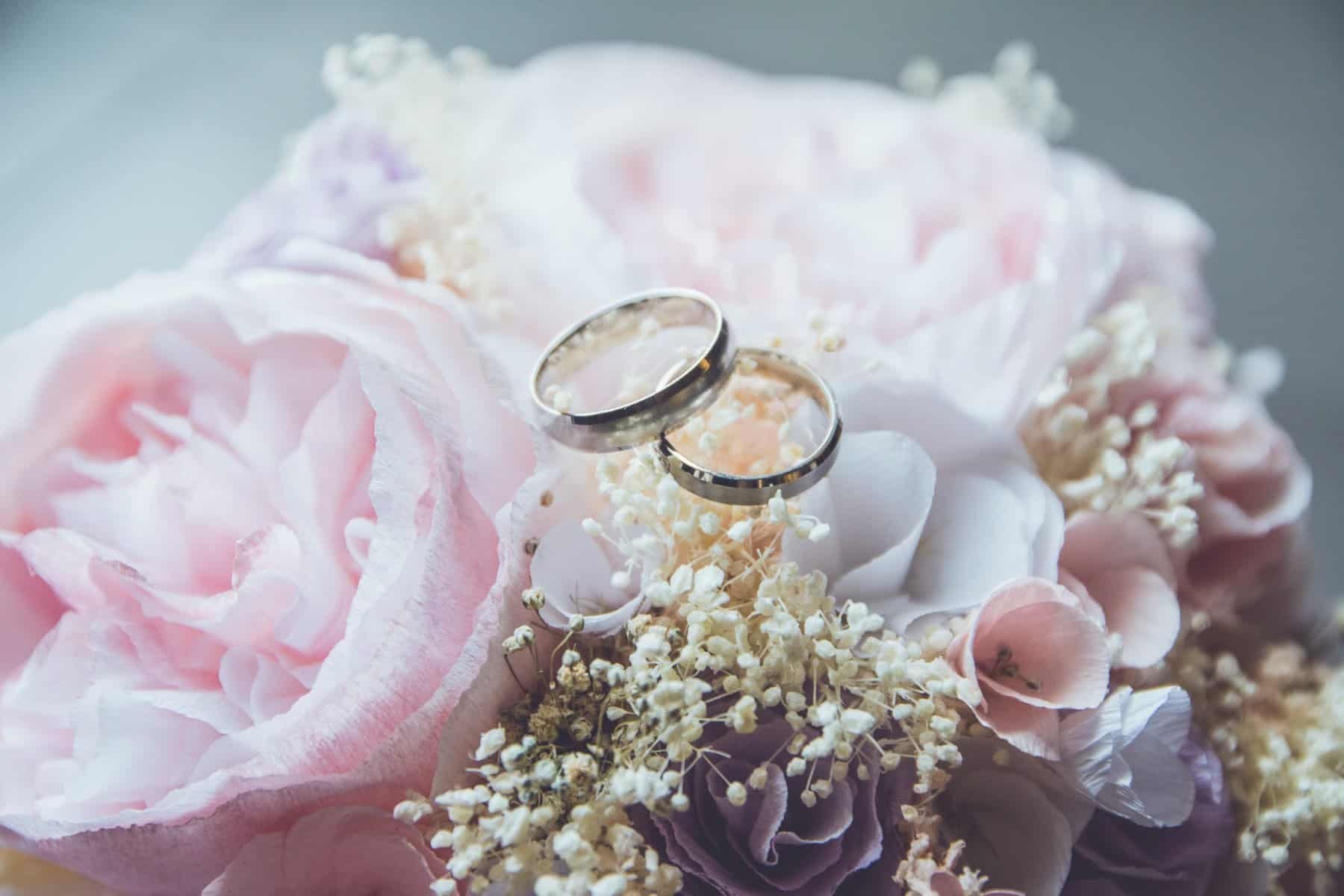 Featured Image: bridal bouquet of pink roses with the bride and groom's wedding bands laying on top of it
