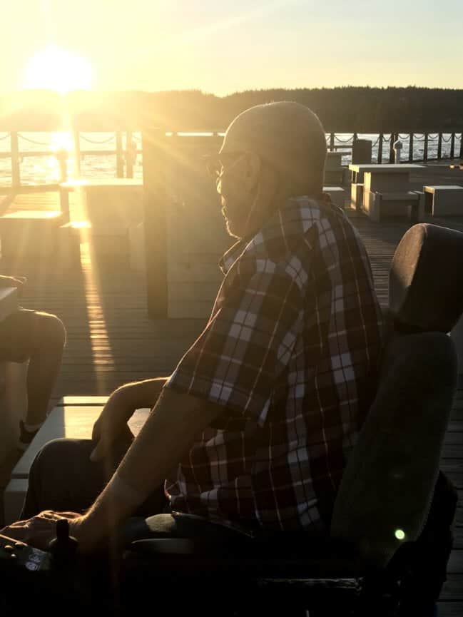 Elderly man wearing oxygen, watching the sunset over the lake from his power wheelchar