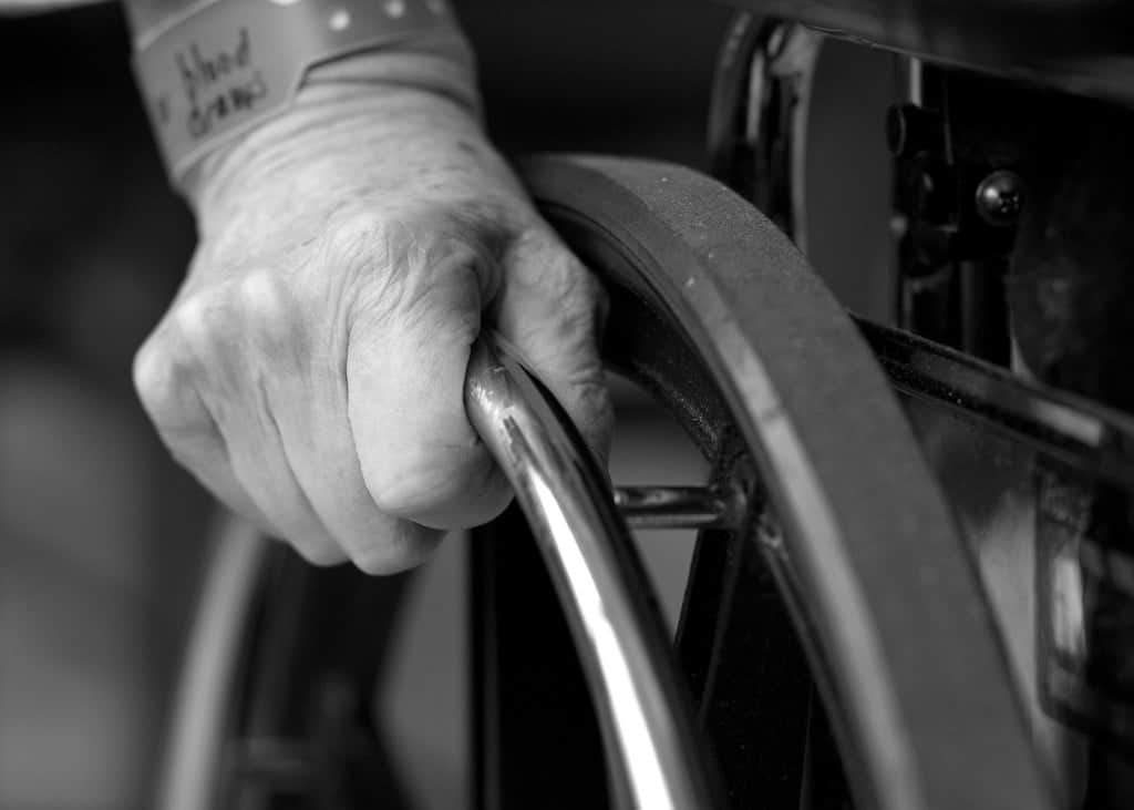 Hand of an elderly person, on the wheel of a wheelchair